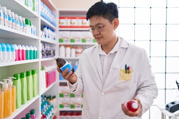 Sticker - Young chinese man pharmacist holding medication bottles at pharmacy