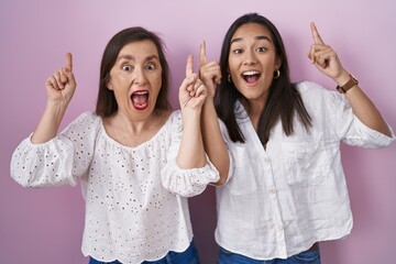 Wall Mural - Hispanic mother and daughter together smiling amazed and surprised and pointing up with fingers and raised arms.