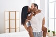 Man and woman interracial couple holding on back standing and kissing at bedroom