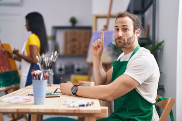 Canvas Print - Hispanic man at painter studio smiling with an idea or question pointing finger with happy face, number one