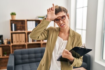 Sticker - Young woman working at consultation office making fun of people with fingers on forehead doing loser gesture mocking and insulting.