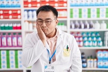 Poster - Chinese young man working at pharmacy drugstore thinking looking tired and bored with depression problems with crossed arms.