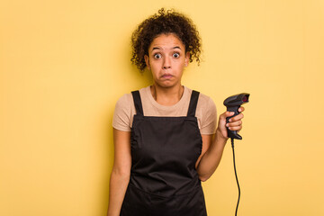 Young brazilian work woman holding a hand sticker price label machine isolatedYoung brazilian woman holdishrugs shoulders and open eyes confused.