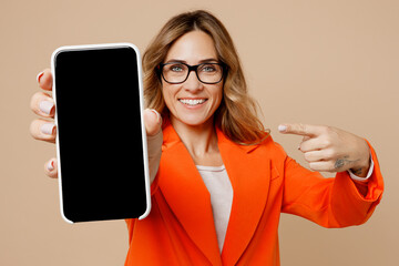 Young fun employee business woman corporate lawyer in classic formal orange suit glasses work in office hold use mobile cell phone show blank screen workspace area isolated on plain beige background