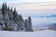 Winter mountains panorama with snow cannons, ski slopes and ski lifts among spruce forest on a background of mountain ranges and cloudy sky in Germany Hessen Rhoen on the Wasserkuppe
