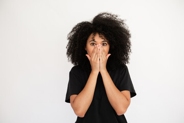 Wall Mural - Amazed young woman covering her face with hands. Caucasian female model with afro hairstyle and brown eyes in black T-shirt closing her face hearing shocking news. Emotion, astonishment concept