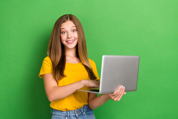 Poster - Photo of positive smiling brown hair teenager girl wear orange t-shirt hold laptop browsing useful information isolated on green color background