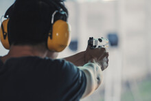 Asian Shooter Man Wearing Noise Canceling Headphones And Black Clothes Practicing Shooting Short Gun At The Shooting Range. Shooting Sports For Meditation And Self-defense, Recreational Activities.