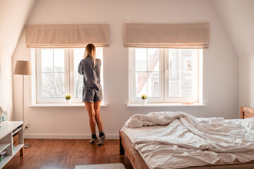 Wall Mural - Young woman stands near the window on a sunny morning. Morning exercise and meditation. Awakening from sleep. Good morning magic morning. Women's recreation