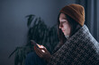 © MZaitsev - A warmly dressed young woman uses a smartphone in a dark room without electricity and heating. Emergency shutdown. Close up.