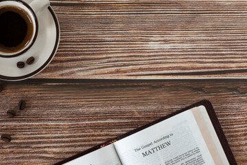 Wall Mural - Open holy bible book Matthew gospel with coffee cup on wooden background. Copy space. Top table view. Studying Christian Scriptures, biblical concept.