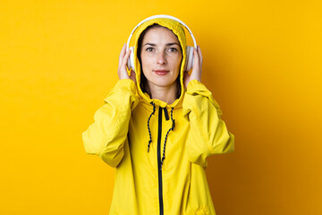 Wall Mural - Young woman in headphones in a yellow jacket on a yellow background.