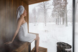 woman in white towel relaxing in sauna and enjoying winter landscape