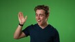 Portrait of happy young man 20s smiling scream and shout calling waving inviting with hands at mouth say hey you isolated on solid green screen background 