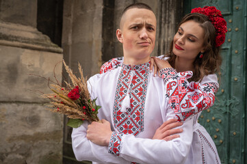 Wall Mural - A young, emotional, happy couple in love, a family walks through the old city of Lviv in Ukrainian embroidered shirts, holding hands against the background of the old city. Young people hug in the old