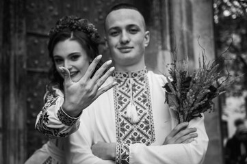 Wall Mural - black and white photo, Emotional portrait of happy young couple in love, family hugging, holding hands, running in Lviv city in traditional Ukrainian shirts. Young people hug in the old town of Lviv