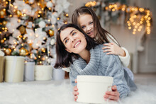 Portrait Of Happy Mother And Daughter Spend Free Time Together, Embrace Each Other, Have Pleasant Smiles, Hold Wrapped Present Boxes, Celebrate New Year Or Christmas Together. Holidays Concept
