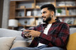 © sofiko14 - Attractive man in red checkered shirt sitting on couch and using modern smartphone indoors. Male freelancer taking break during working process at home.