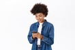 Smiling african american woman using mobile phone, holding telephone and looking happy, standing over white background
