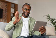 Glad Happy Middle Aged Black Guy In Glasses Waving Hand At Digital Tablet Webcam, Say Hello, Hi, Make Greeting Gesture
