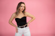 © Татьяна Волкова - Young blond fashionable, confident woman with hands on hips wearing trendy black top and white jeans on pink background