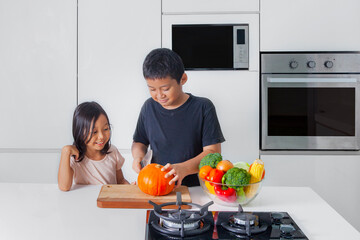 Two cute little kids cutting a pumpkin in kitchen