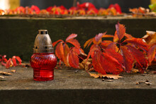 Red Grave Lantern And Fallen Leaves On Stone Surface In Cemetery, Space For Text