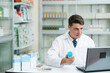 © ijeab - Male pharmacist working in modern pharmacy using laptop.