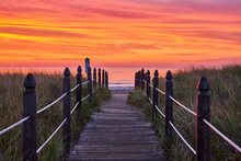 Boardwalk Path Leading Directly To Maine East Coast Ocean View During Stunning Orange And Red Sunrise