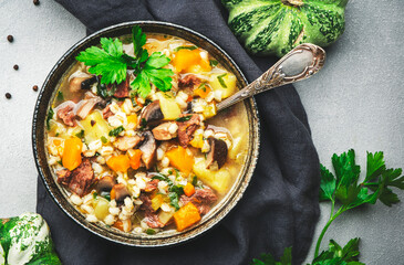 Winter comfort food. Warming high-calorie soup with pumpkin, mushrooms, potato, beef and barley. Gray table background, top view, copy space