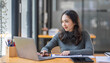 © David - Freelancer Happy business Asian woman in knitwear taking notes at laptop sitting at desk office, finance concept.
