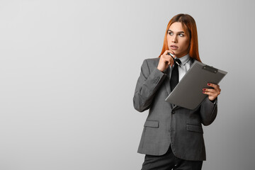 Wall Mural - Thoughtful transgender secretary with clipboard on grey background