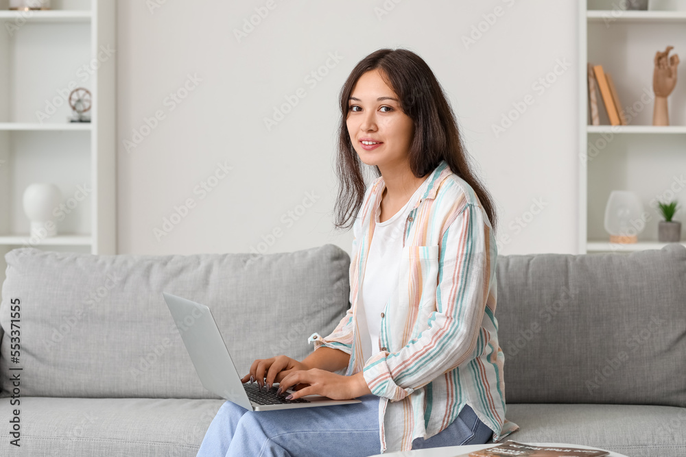 Young Asian woman using laptop on sofa at home