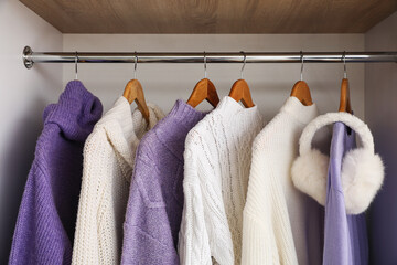 Warm knitted sweaters and ear muffs hanging in wardrobe, closeup