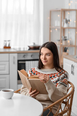 Wall Mural - Young woman reading book at dining table in kitchen