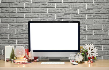 Computer with Christmas decor, lamp and candles on table near grey brick wall