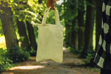 Close-up of Unrecognizable female hand holding cotton eco bag in park. Reusable eco bag in park. Mock up Sustainable lifestyle. Plastic free zero waste free living. Go green Environment protection