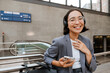 Asian woman in headphones using mobile phone while standing outdoors
