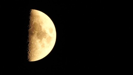 Wall Mural - A glowing golden huge half moon seen from earth through the atmosphere against a starry night sky. A large moon moves across the sky, the moon moving from the left frame to the right.