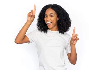 Wall Mural - Cheerful multiracial woman pointing up at ads. Excited young female model with dark curly hair in white T-shirt looking at camera, smiling, showing two options with fingers. Advertisement concept