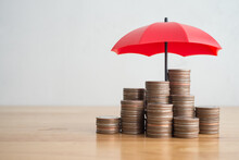 Stacked Coins Is Protected By Red Umbrella On Wooden Table White Wall Background Copy Space. Assets Wealth, Money Saving Or Money Investment Protection, Security By Insurance Concept. Risk Management.