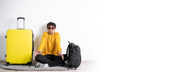 Wall Mural - Young traveler man with suitcase looking in camera with raised eyebrows and surprised face expression isolated over white background.