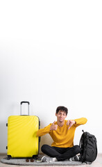 Wall Mural - Young traveler man making thumbs up and thumbs down hands sign while sitting with suitcase over isolated white background