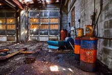 Interior Abandoned Mechanic Shop Garage With Dirty Ground And Old Lubricant Barrels