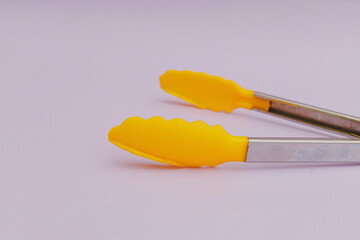 Wall Mural - Yellow pasta tongs on purple background