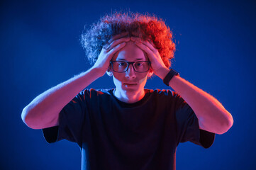 Poster - Young man with curly hair is indoors illuminated by neon lighting