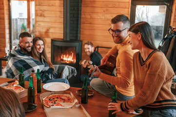 Wall Mural - Near the fireplace. Group of friends is having good weekend indoors in the wooden building together