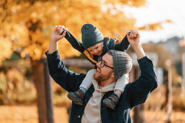 Wall Mural - Front view. Son is on the dad's shoulders. Father and young son is together outdoors at daytime