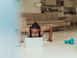 © .shock - Young African American man working push-ups in the living room while watching online training on laptop