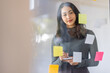 © David - Business female employee with many conflicting priorities arranging sticky notes commenting and brainstorming on work priorities colleague in a modern office.